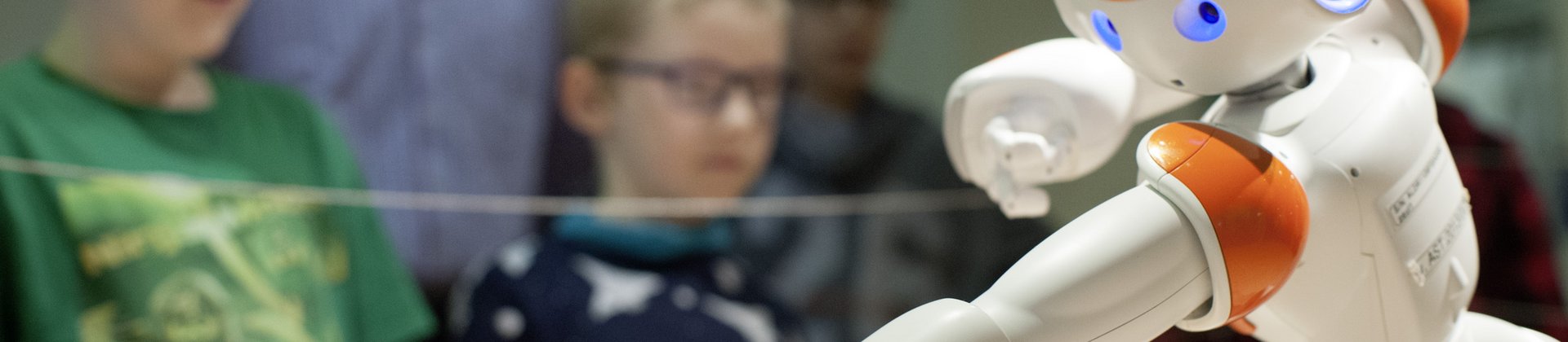 Kinder beobachten einen kleinen Roboter, der sich im Bildvordergrund befindet.