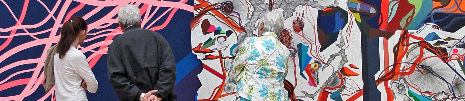 Drei Personen betrachten eine bunte Ausstellungswand.